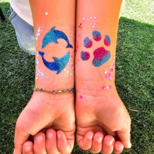 Glitter tattoos of dolphins and a paw print on a girls arms